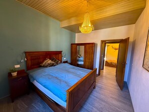 A bedroom with a wooden bed, a nightstand, a mirror, and a chandelier. - Casa Claudia Pieve centro storico (Tremosine)