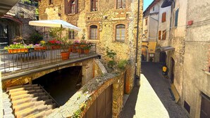 A narrow street with stone buildings, a covered outdoor seating area with tables and chairs, and a staircase leading down to a lower level.
