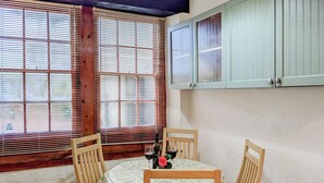 A dining area with a table set for two, wooden chairs, and a window with blinds. - 1 bedroom accommodation in Workington (Workington)