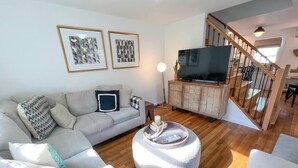 A living room with a sofa, ottoman, and a television on a wooden cabinet.