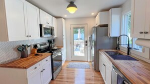 A modern kitchen with white cabinets, a wooden countertop, and a view to the outside.