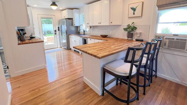 A modern kitchen with a wooden island, white cabinets, and a herringbone backsplash.