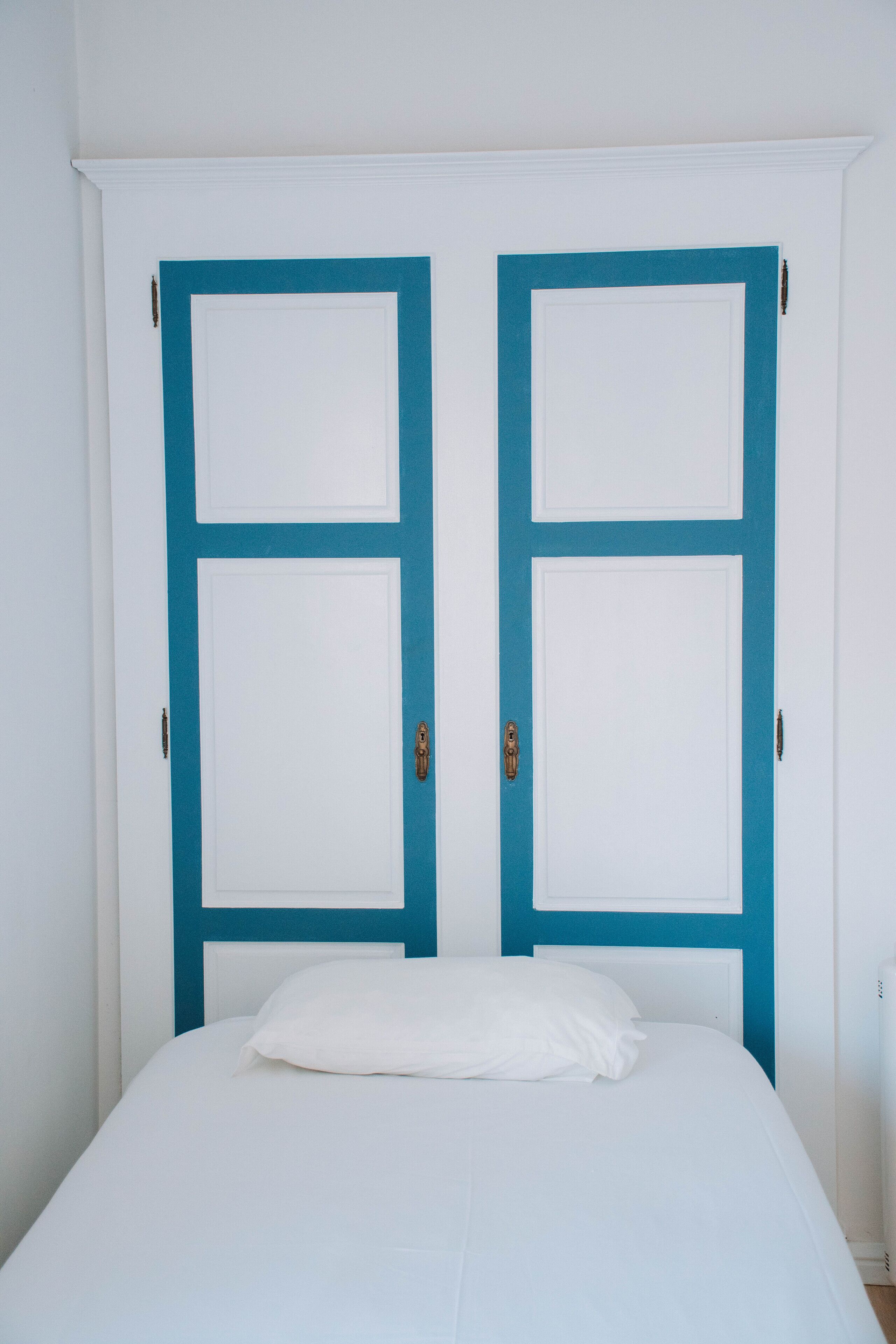 Una habitación con una cama, dos puertas con marco azul y paredes blancas.