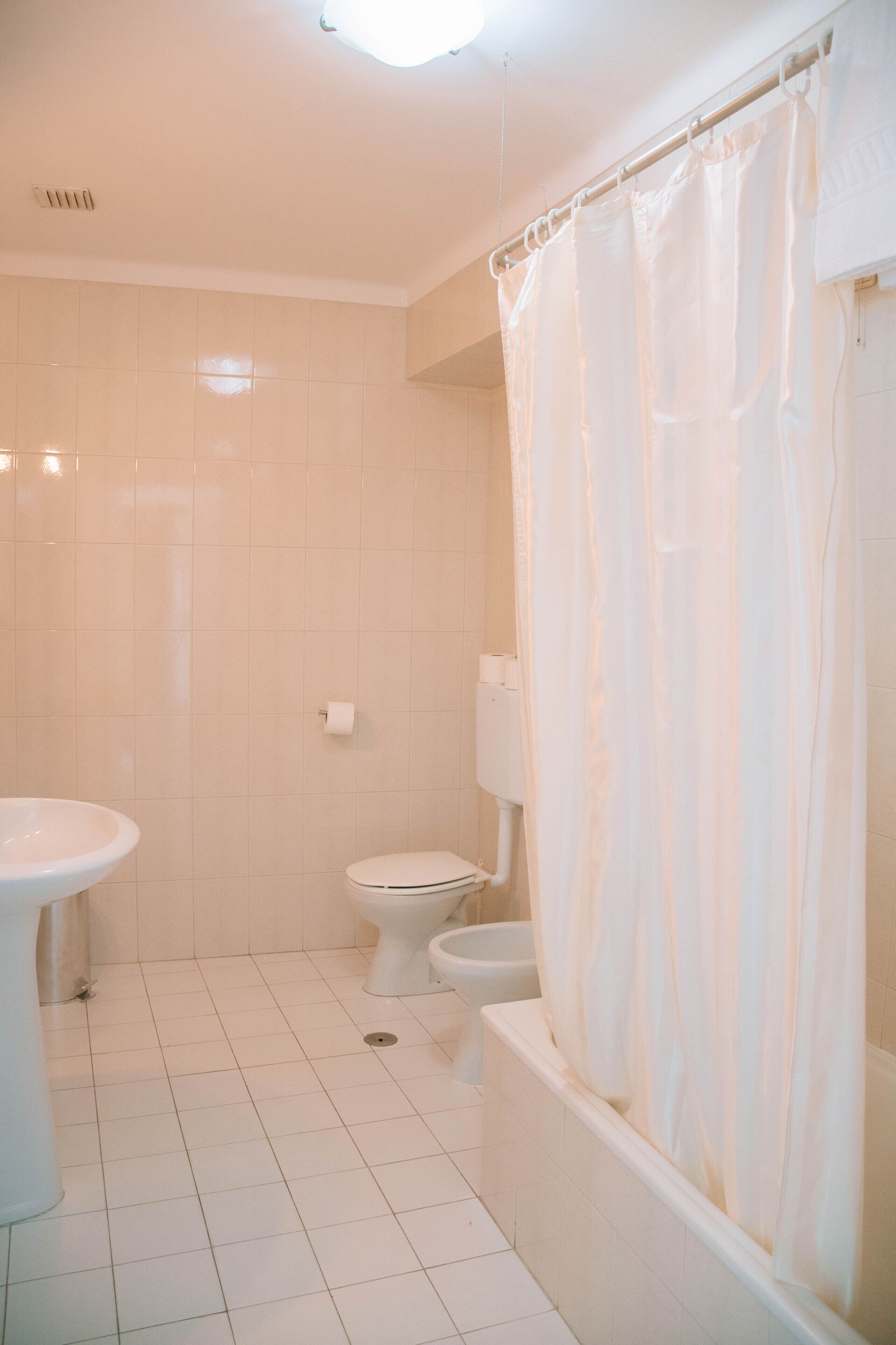 Ein Badezimmer mit weißen Fliesen, einer Toilette, einem Waschbecken und einer Badewanne mit Duschvorhang.