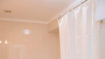 Ein Badezimmer mit weißen Fliesen, einer Toilette, einem Waschbecken und einer Badewanne mit Duschvorhang.