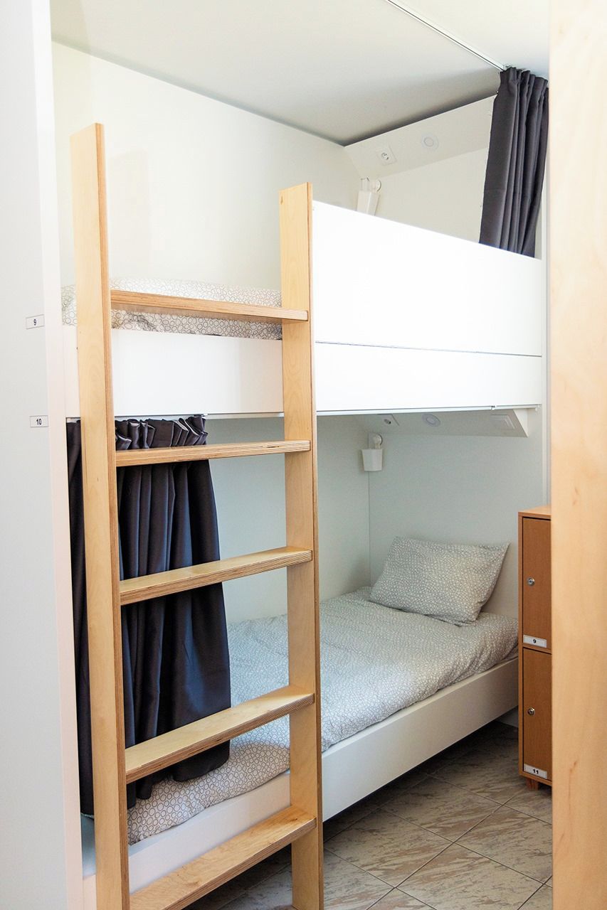 A bunk bed with a wooden ladder, a single bed below, and a small cabinet.