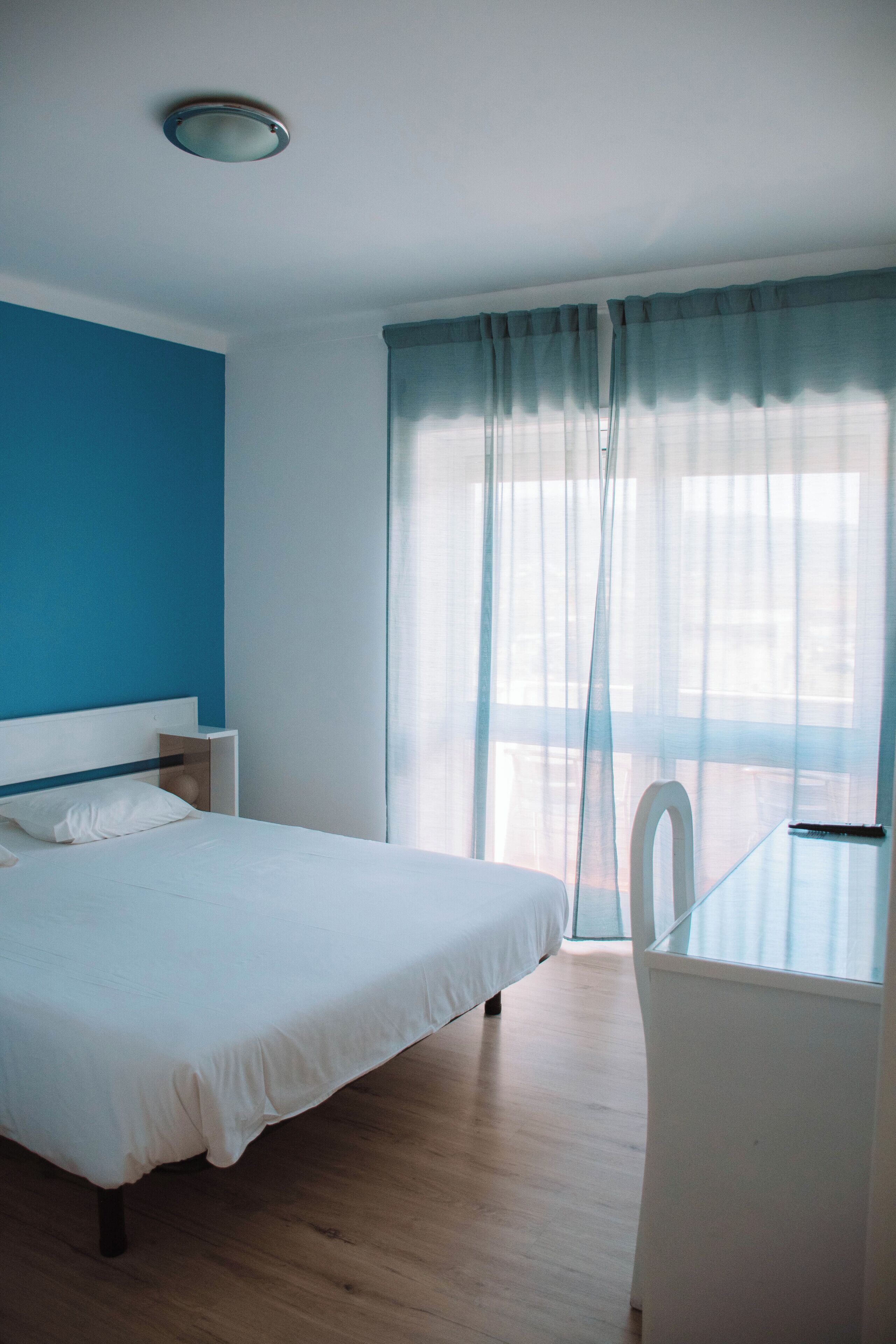Una camera da letto con un letto, un comodino e una sedia vicino a una finestra con tende leggere.