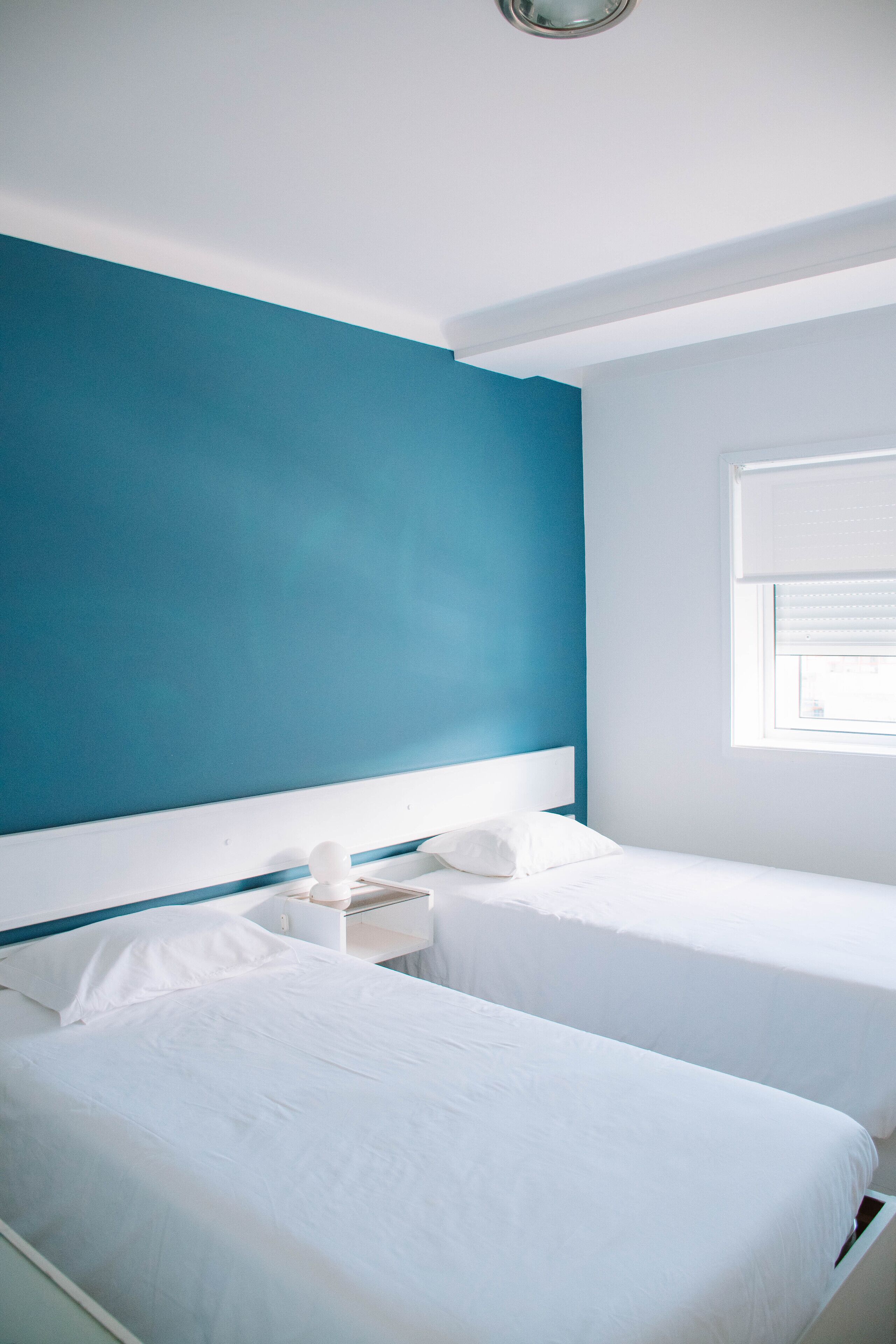 A room with two beds, a white nightstand, and a window with blinds.