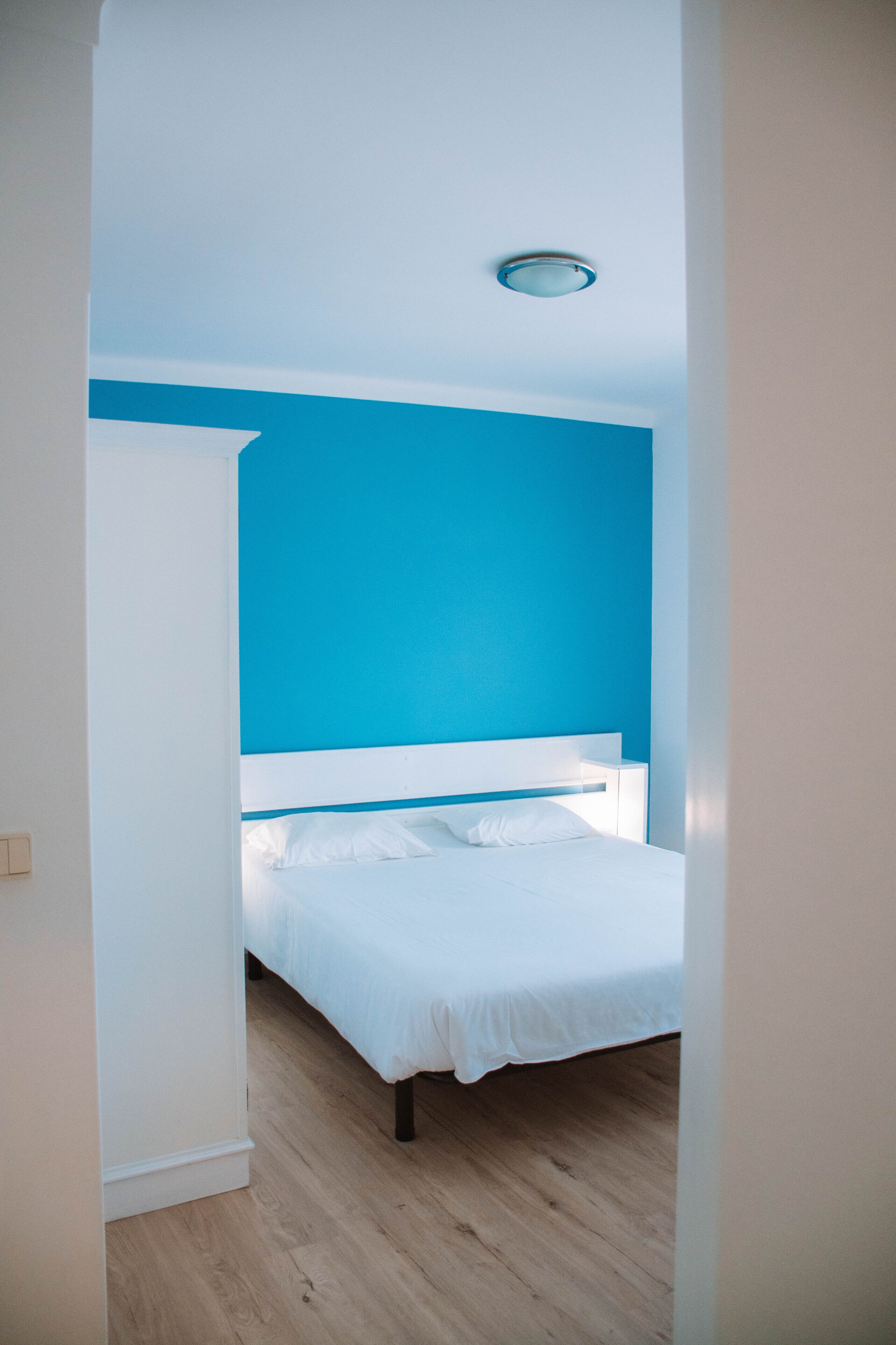 A bedroom with a white bed, a blue accent wall, and a wooden floor.