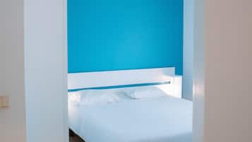 A bedroom with a white bed, a blue accent wall, and a wooden floor.