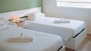 A hotel room with two beds, a nightstand, a bedside table, a window with blinds, and a green wall. - ARCA NOVA GUEST HOUSE & HOSTEL (Caminha)
