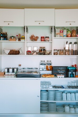 A kitchen with white cabinets, shelves stocked with food items, and a coffee station. - ARCA NOVA GUEST HOUSE & HOSTEL (Caminha)
