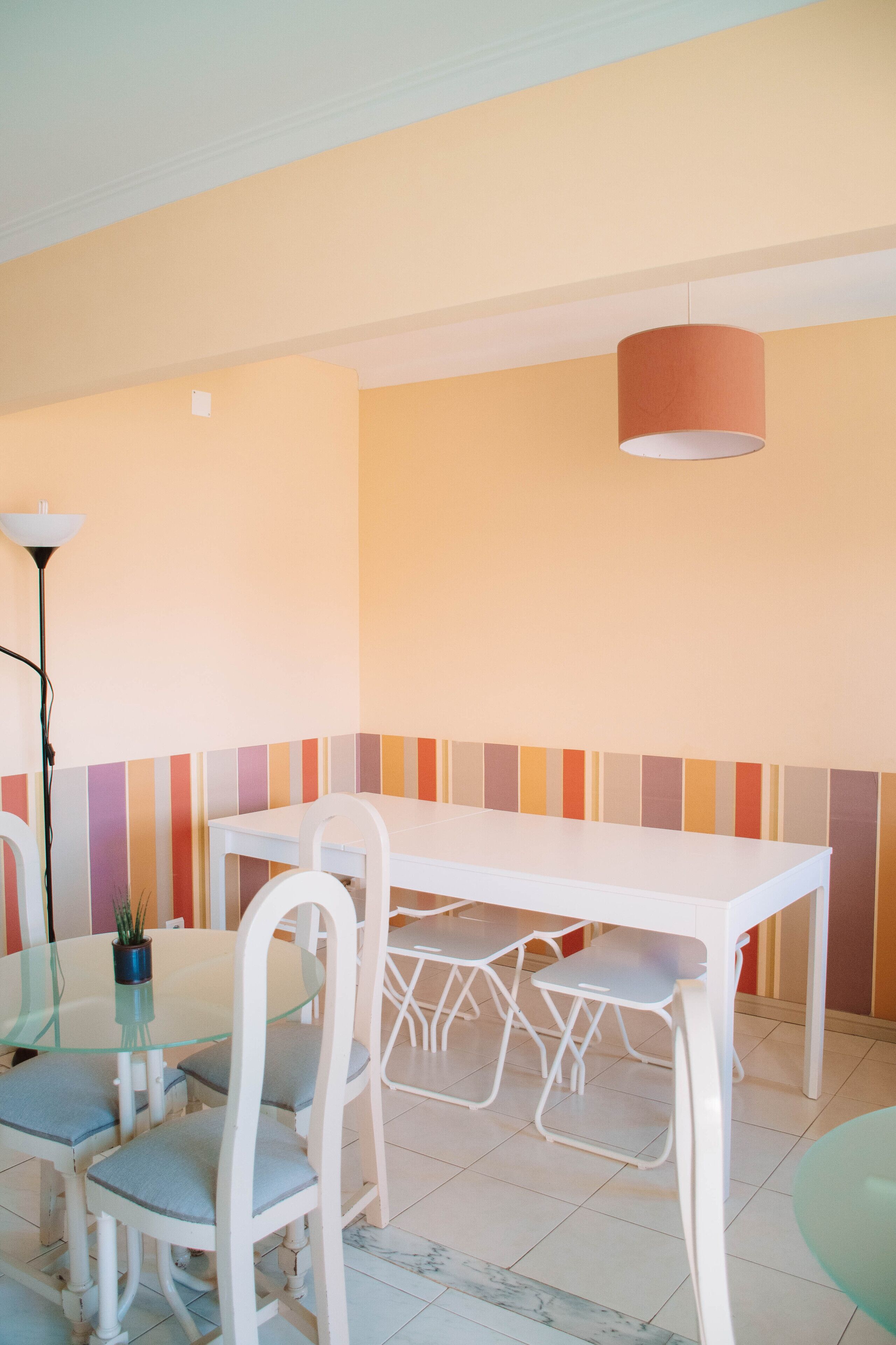 A dining area with a white table and chairs, a hanging lamp, and a striped wall.