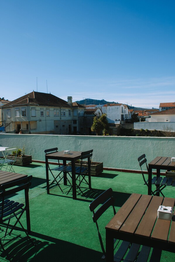 An outdoor seating area with tables and chairs, a green artificial turf floor, and a view of buildings in the background. - ARCA NOVA GUEST HOUSE & HOSTEL (Caminha)