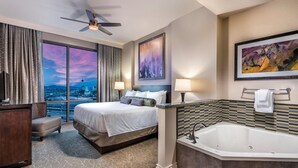 Habitación de hotel con una cama grande, zona de estar, bañera y vistas a la ciudad.