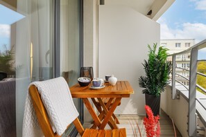 Uma varanda com uma mesa de madeira, uma toalha branca e um vaso com planta.