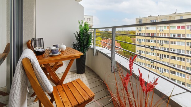 A balcony with a wooden table, chairs, and a potted plant. - Sun Towers Lux by Renters Prestige (Swinoujscie)