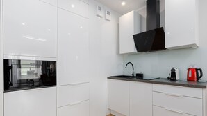 A modern kitchen with white cabinets, a black range hood, a sink, and a red kettle. - Sun Towers Lux by Renters Prestige (Swinoujscie)