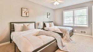 A bedroom with two beds, a ceiling fan, and a large window with blinds.