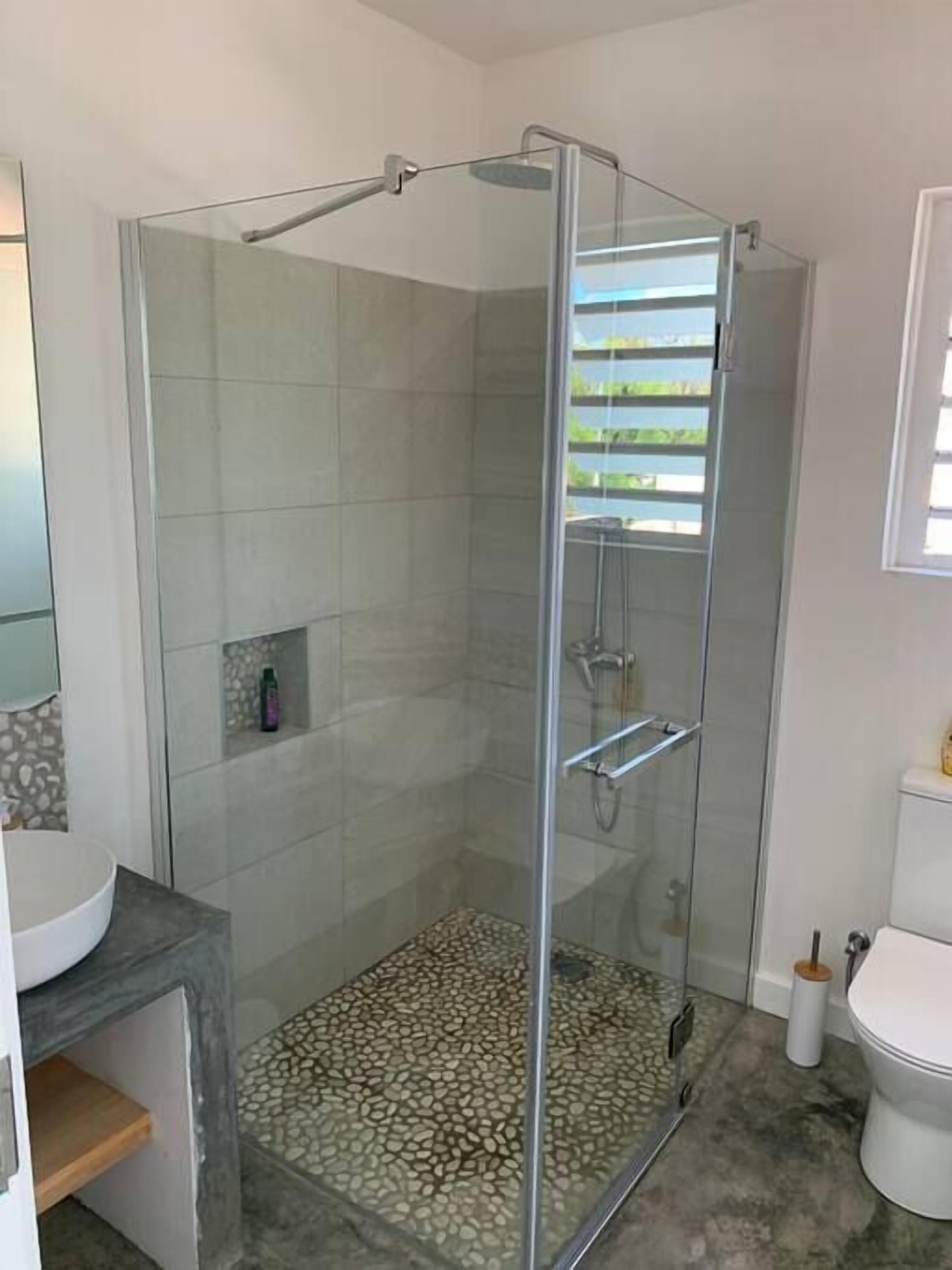 A modern bathroom with a glass-enclosed shower, a round sink, and a toilet.