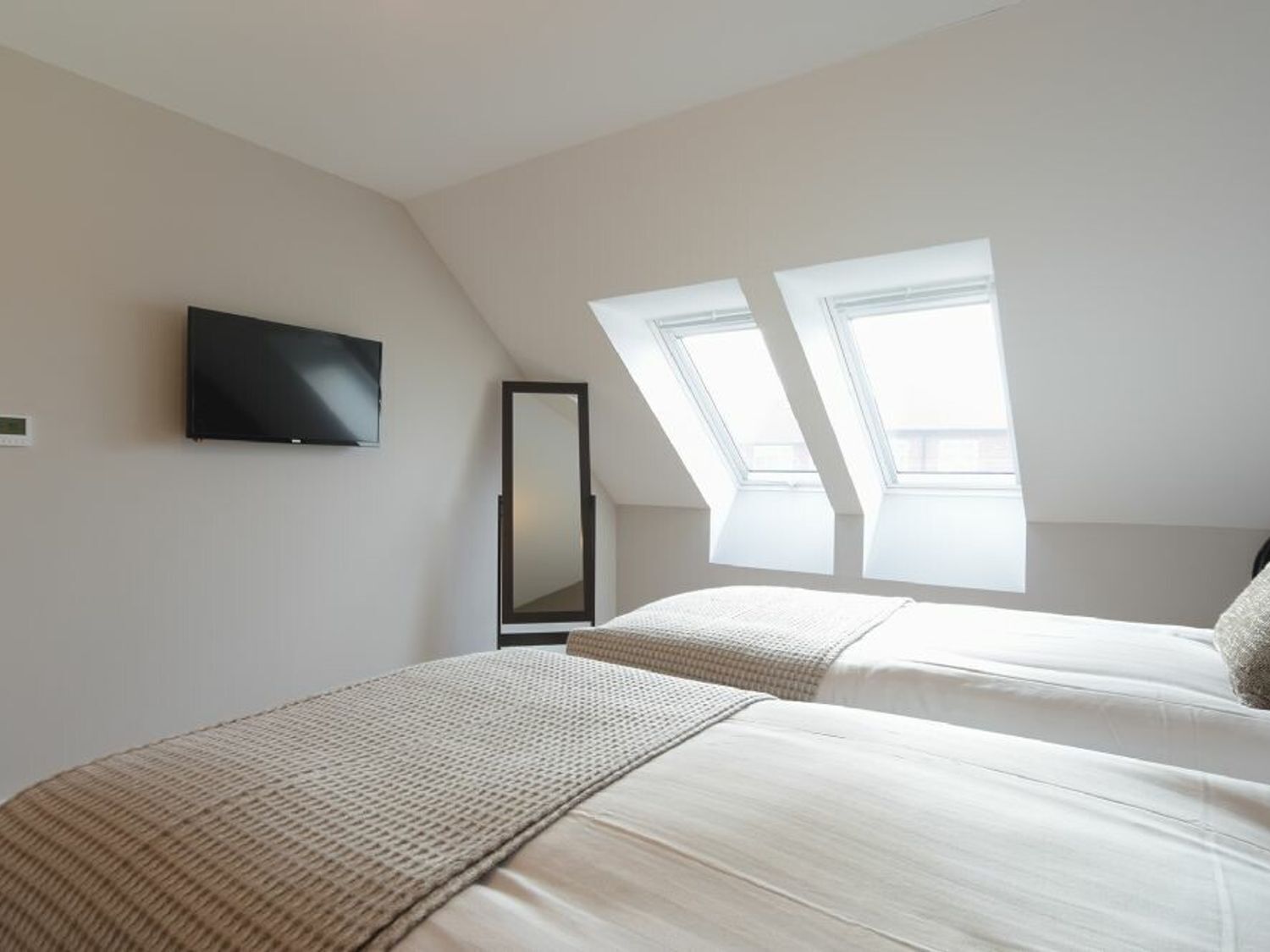 Quarto com duas camas, televisão, espelho e claraboias.