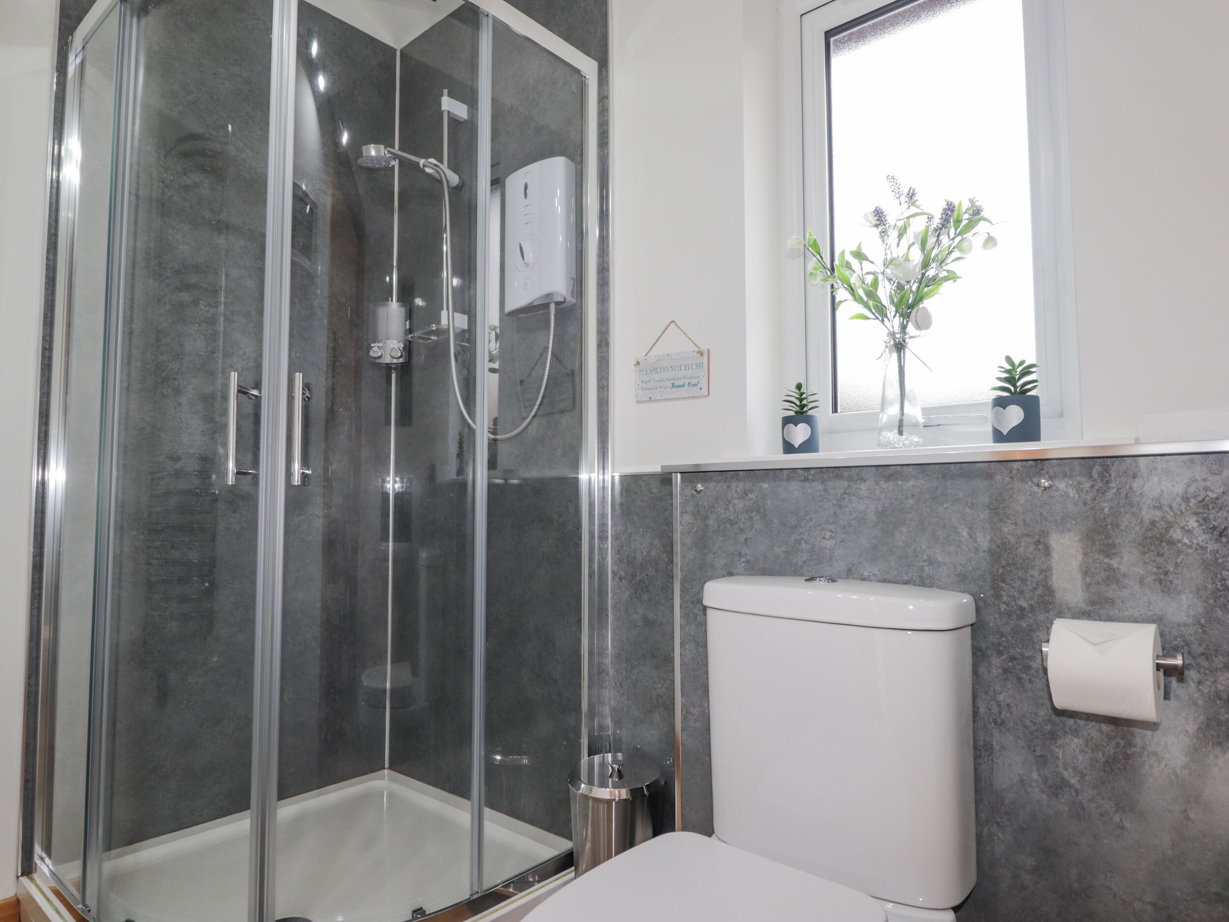 A modern bathroom with a glass-enclosed shower, a toilet, and a window with a view of flowers.