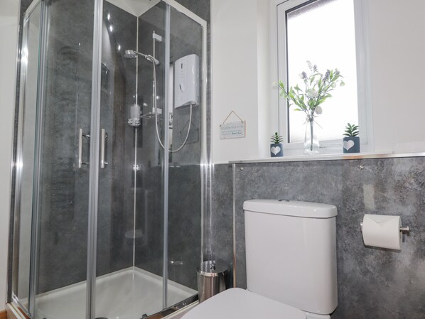 A modern bathroom with a glass-enclosed shower, a toilet, and a window with a view of flowers. - Pebble Cottage (Portree)