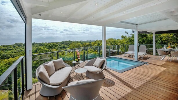 Une terrasse extérieure moderne avec une piscine, un espace salon et une vue sur la forêt.