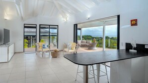 Un vaste espace de vie avec une grande porte-fenêtre coulissante donnant sur un balcon, un téléviseur à écran plat et une cuisine moderne.