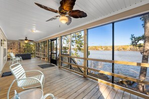 Eine überdachte Terrasse mit Seeblick, Holzliegen und einem Deckenventilator.