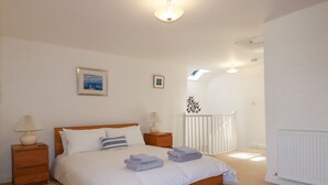 Ein Schlafzimmer mit einem hölzernen Bett, weißer Bettwäsche, zwei Nachttischlampen, einem Nachttisch, einem gerahmten Bild an der Wand und einem weißen Heizkörper.