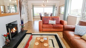 Un salon avec une cheminée, un canapé, une table à manger avec de l’assiette, et une vue sur l’extérieur.