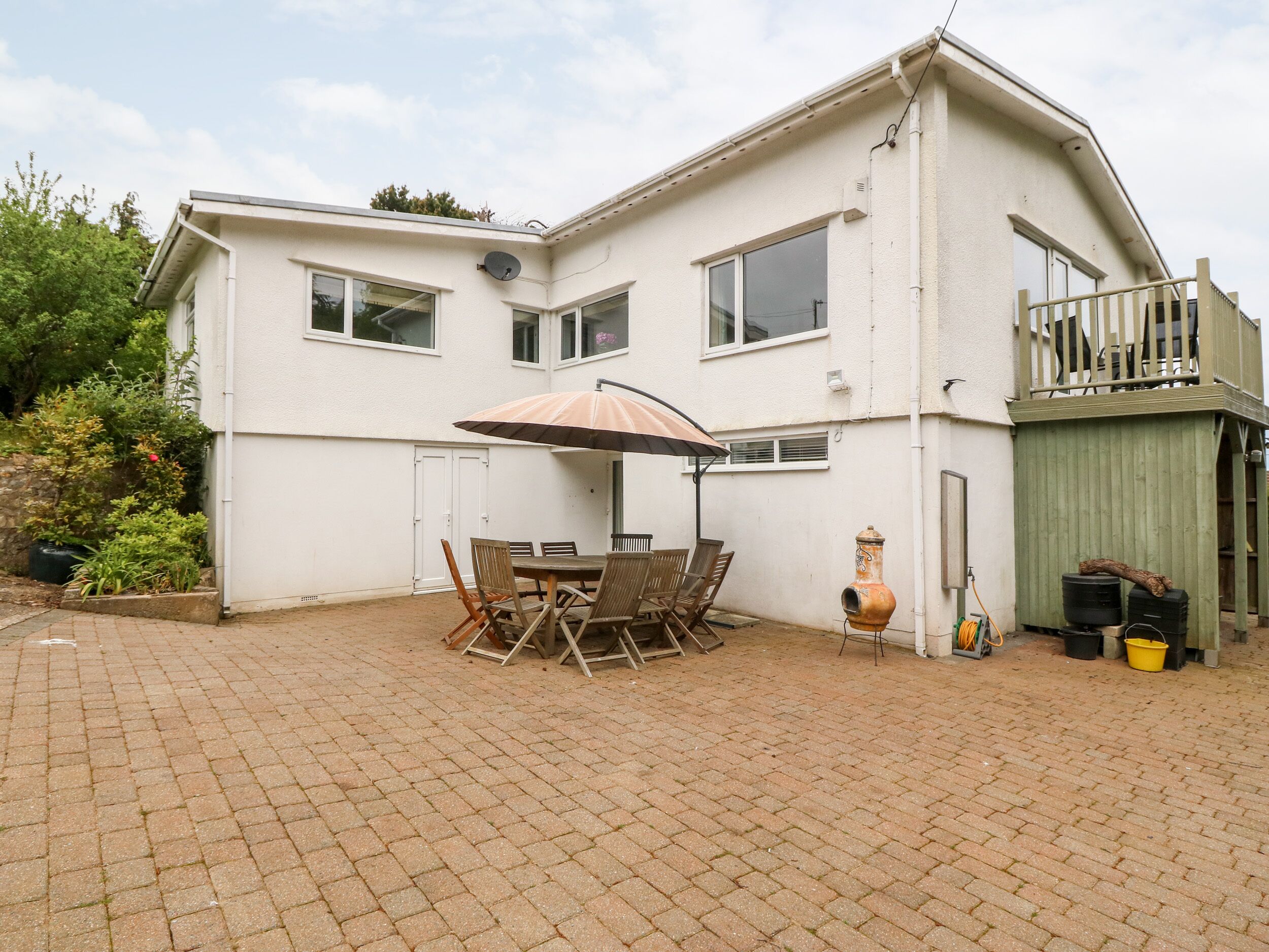 A two-story house with a patio area featuring a table and chairs, a satellite dish, and a small garden.