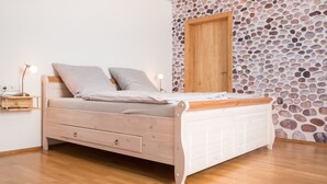 A bed with a wooden frame, two pillows, a bedside table with a lamp, and a stone-patterned wall with a wooden door.