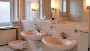 A modern bathroom with two sinks, a bidet, and a large mirror with wall sconces.