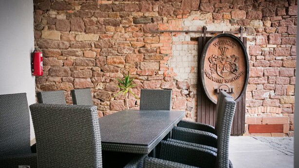 A dining area with a stone wall, wicker chairs, a table, and a wooden barrel with embossed text.