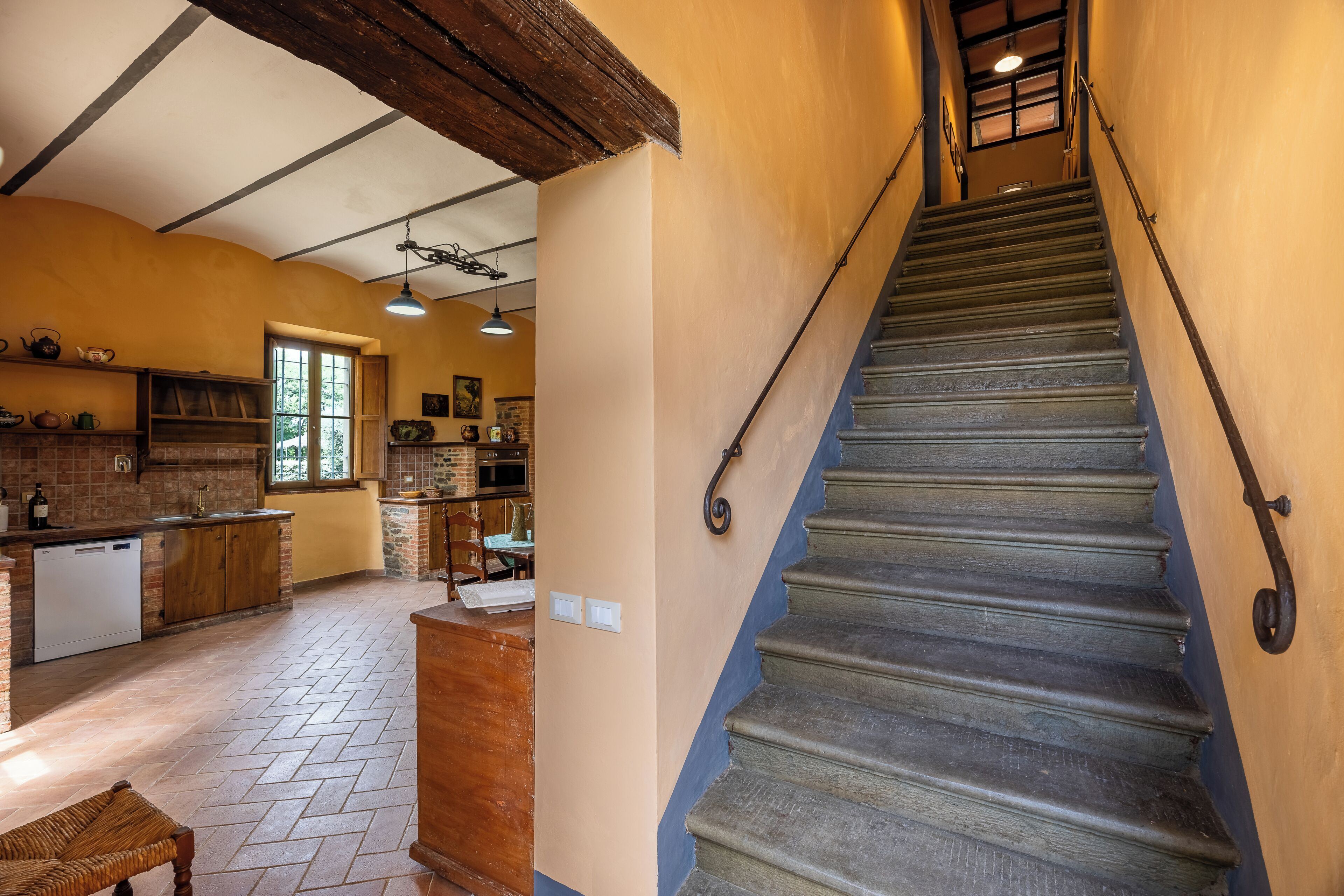 Un escalier avec une rampe en bois et un coin cuisine avec un mur en briques, des placards en bois et une fenêtre.