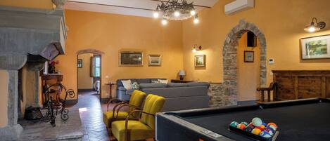 A billiards table, a sofa, a fireplace, and a stone archway in a room with yellow walls and a tiled floor.
