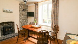 A dining area with a stone fireplace, wooden table, and chairs. - Myrtle Villa (Knighton)