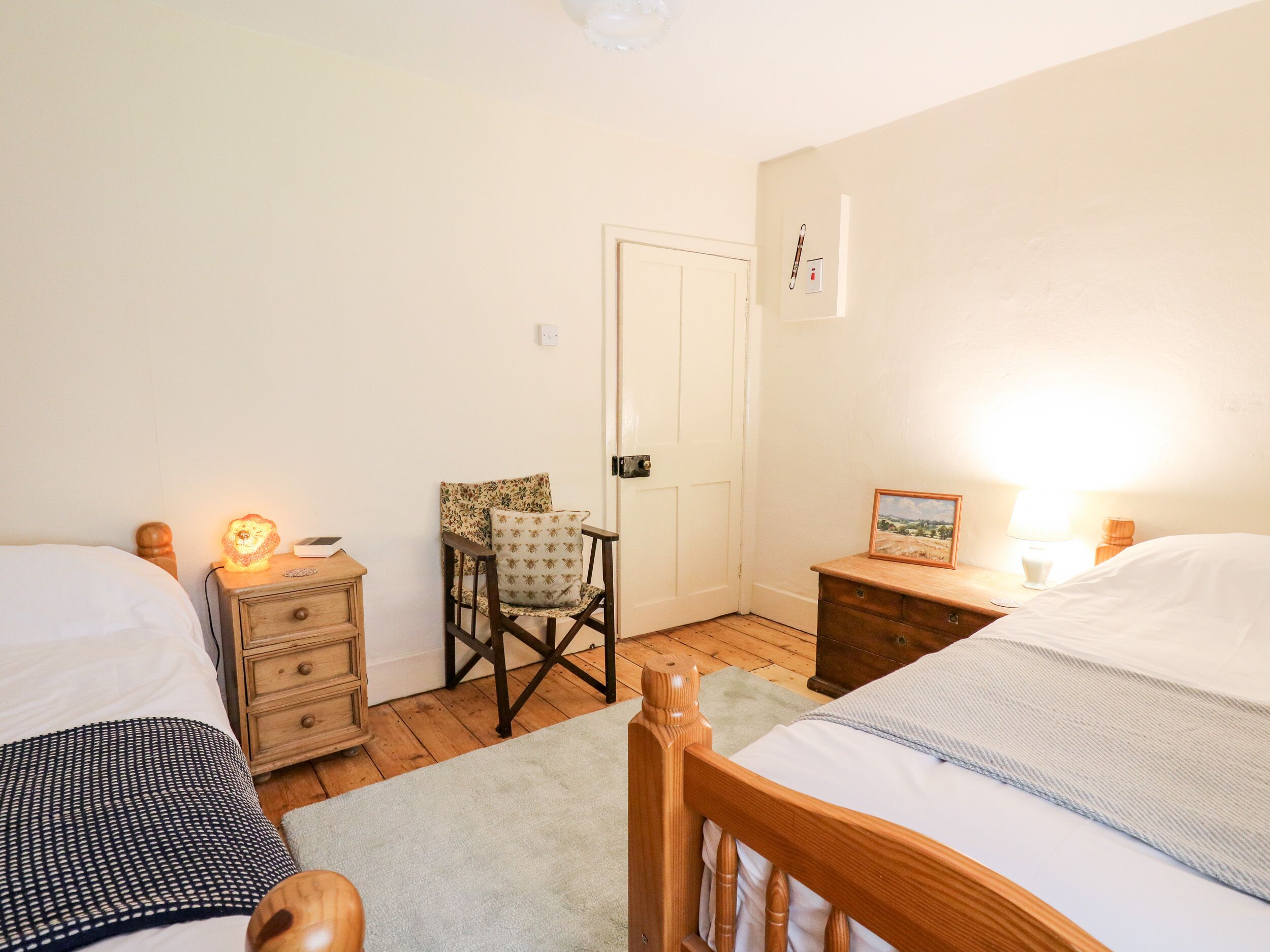 A cozy bedroom with two single beds, a wooden dresser, a chair, and a nightstand with a lamp.