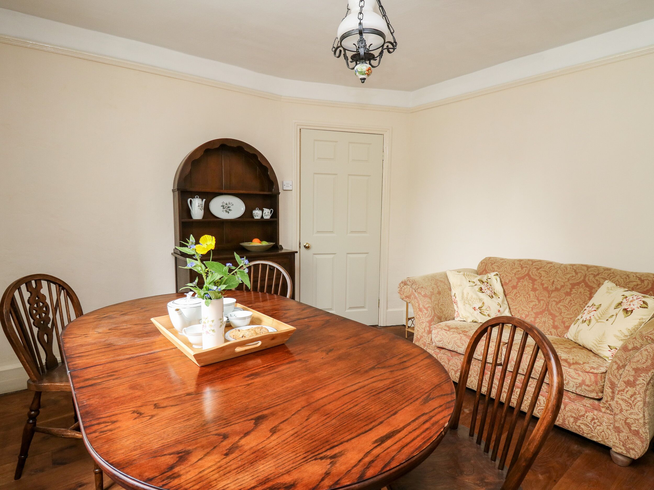 A dining room with a wooden table, chairs, a floral vase, and a patterned sofa.