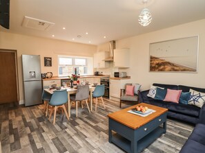 A modern kitchen with a refrigerator, stove, and dining area with chairs and a table. - Lonnon Cottage (Alnwick)