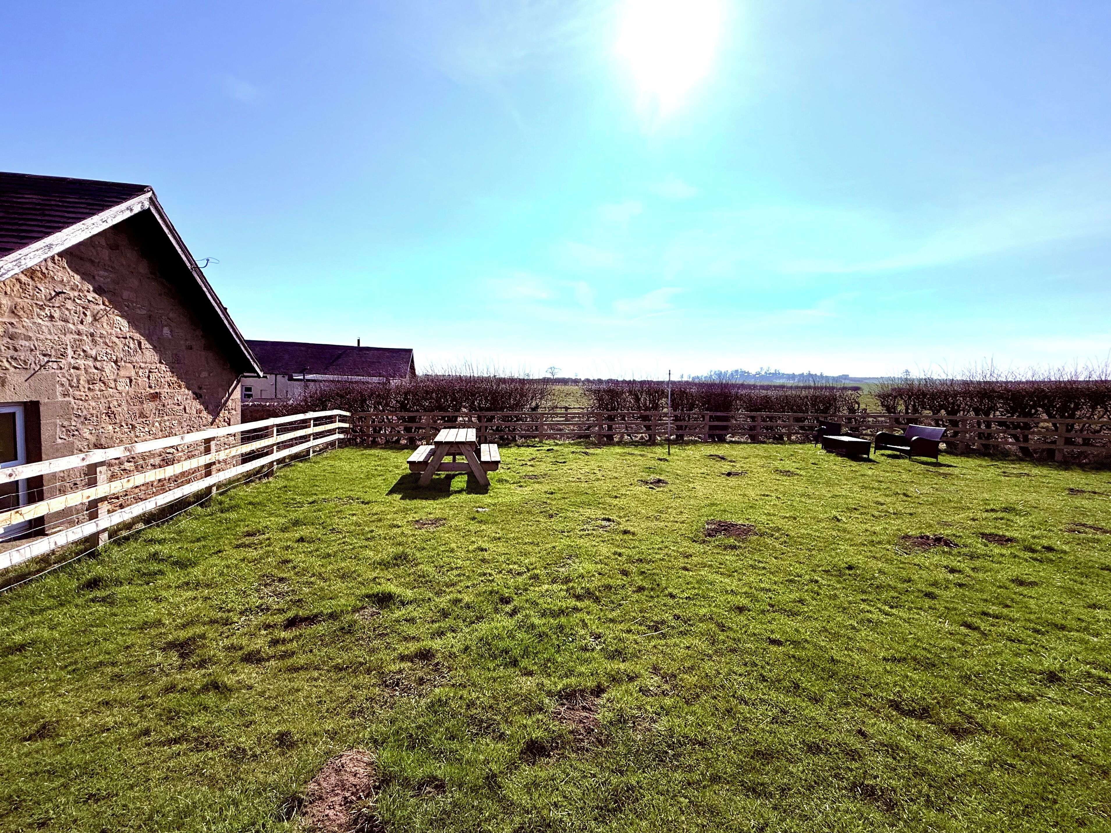 A stone building with a white fence, picnic tables, and a grassy field.