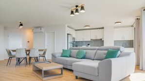 A modern living room with a grey sofa, a coffee table, and a dining area with chairs and a table. - Banana Tree (Camara de Lobos)