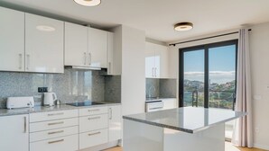 A modern kitchen with white cabinets, granite countertops, and a large island. - Banana Tree (Camara de Lobos)