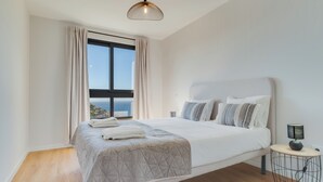 A modern bedroom with a large bed, a bedside lamp, and a view of the sea. - Banana Tree (Camara de Lobos)