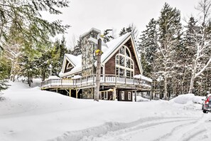Un grand chalet à plusieurs étages, doté d’une façade en pierre, de balcons en bois et surplombant un paysage enneigé.