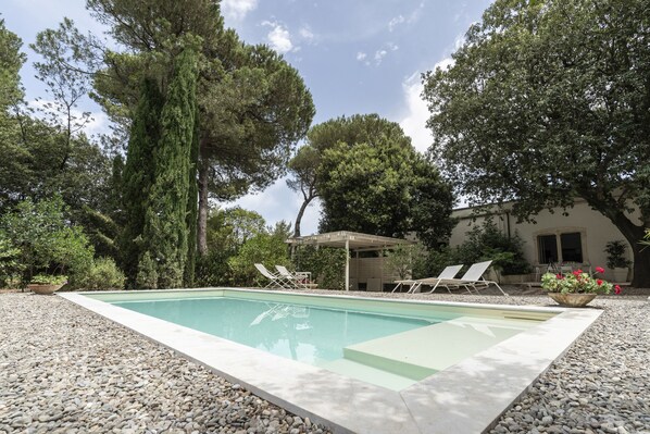 Relax by the serene pool surrounded by lush trees and a traditional building in the background.