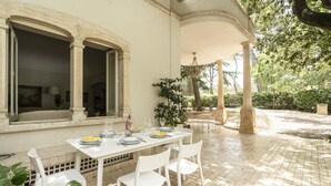 An outdoor dining area with a white table set for four, surrounded by white chairs, under a covered patio with stone flooring. - Villa Manfredi by Wonderful Italy (Fasano)