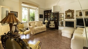 A living room with a fireplace, a large window, and a collection of bookshelves. - Villa Manfredi by Wonderful Italy (Fasano)